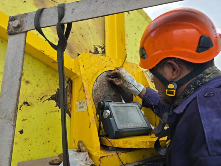 BTS technician inspecting a yellow drilling rig component with a digital inspection instrument